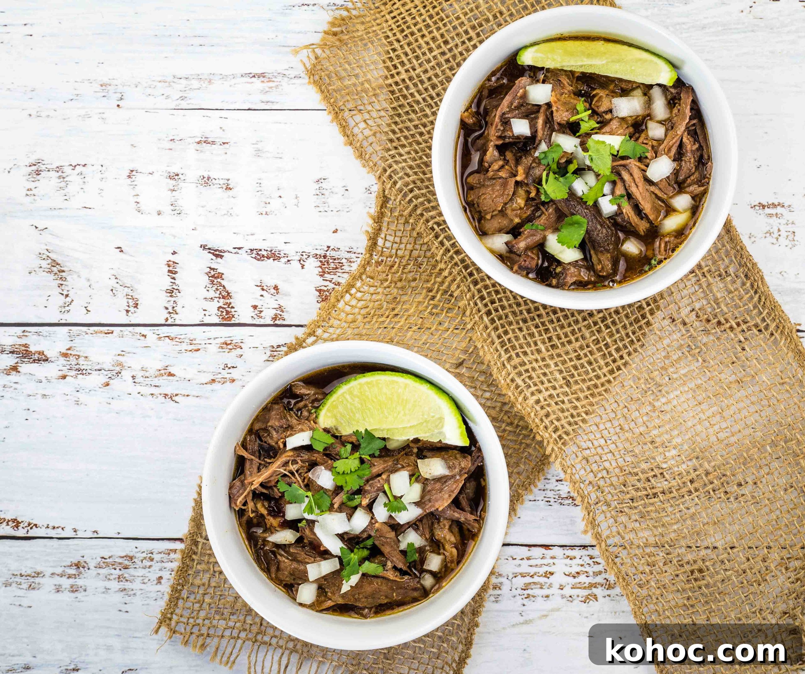 23 Dump-and-Go Slow Cooker Recipes That Taste Homemade 16 Two white bowls filled with slow cooker birria garnished with fresh lime wedges.