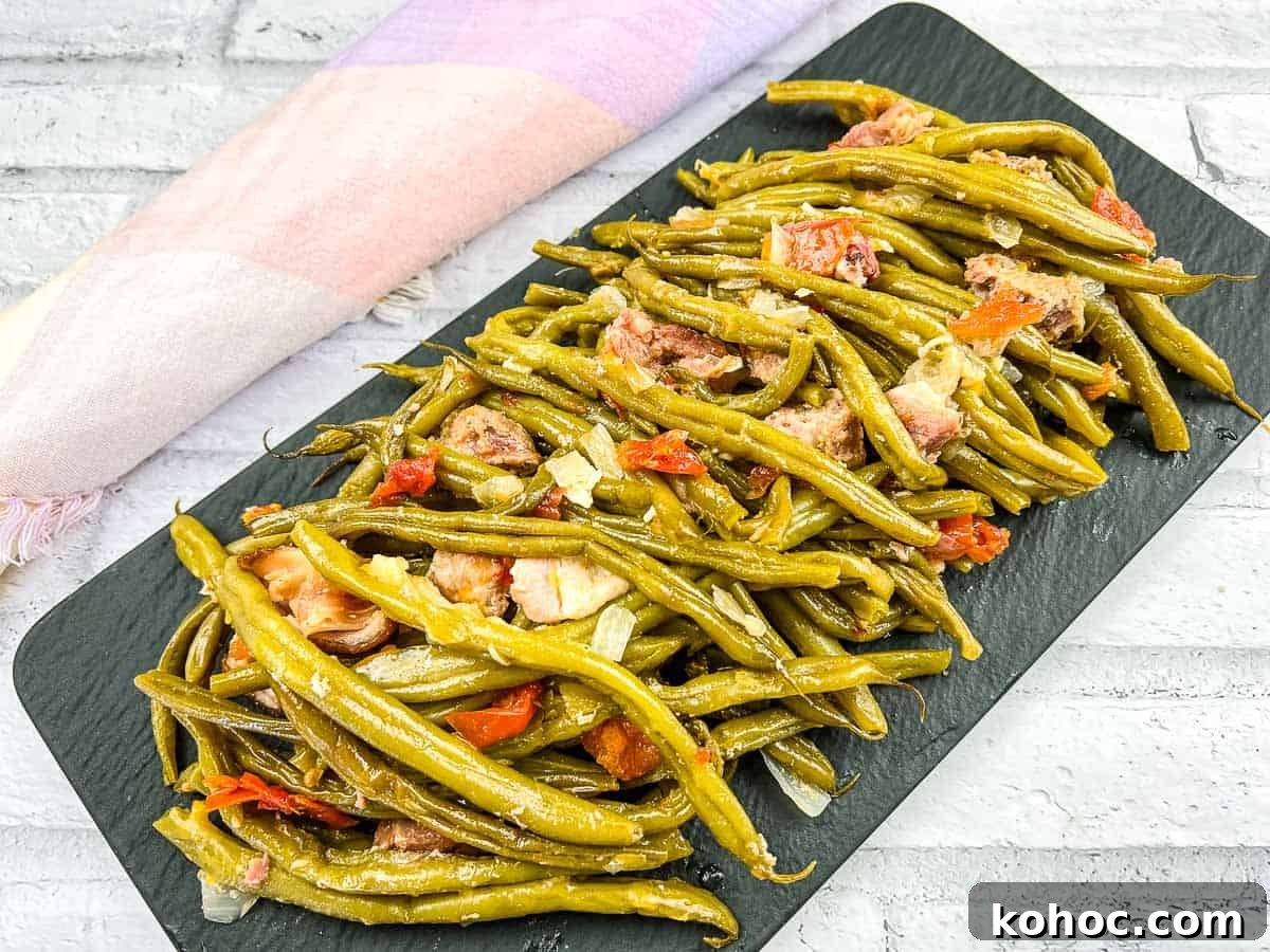 23 Dump-and-Go Slow Cooker Recipes That Taste Homemade 21 A plate of cooked Southern Green Beans with sliced sausages and tomato pieces on a white dish, placed near a sunflower.