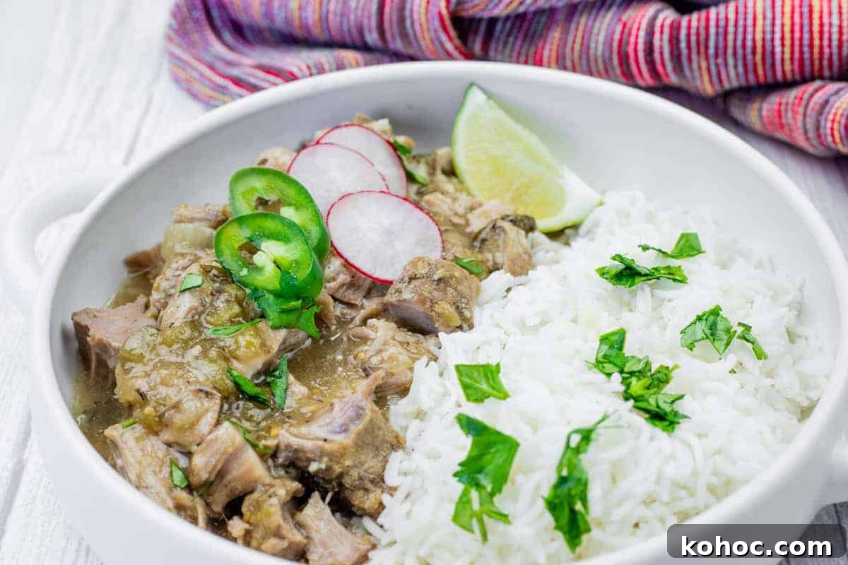 23 Dump-and-Go Slow Cooker Recipes That Taste Homemade 8 A bowl of white rice and green chili verde garnished with cilantro, radish slices, jalapeño, and a lime wedge, set on a white surface with a colorful cloth in the background.