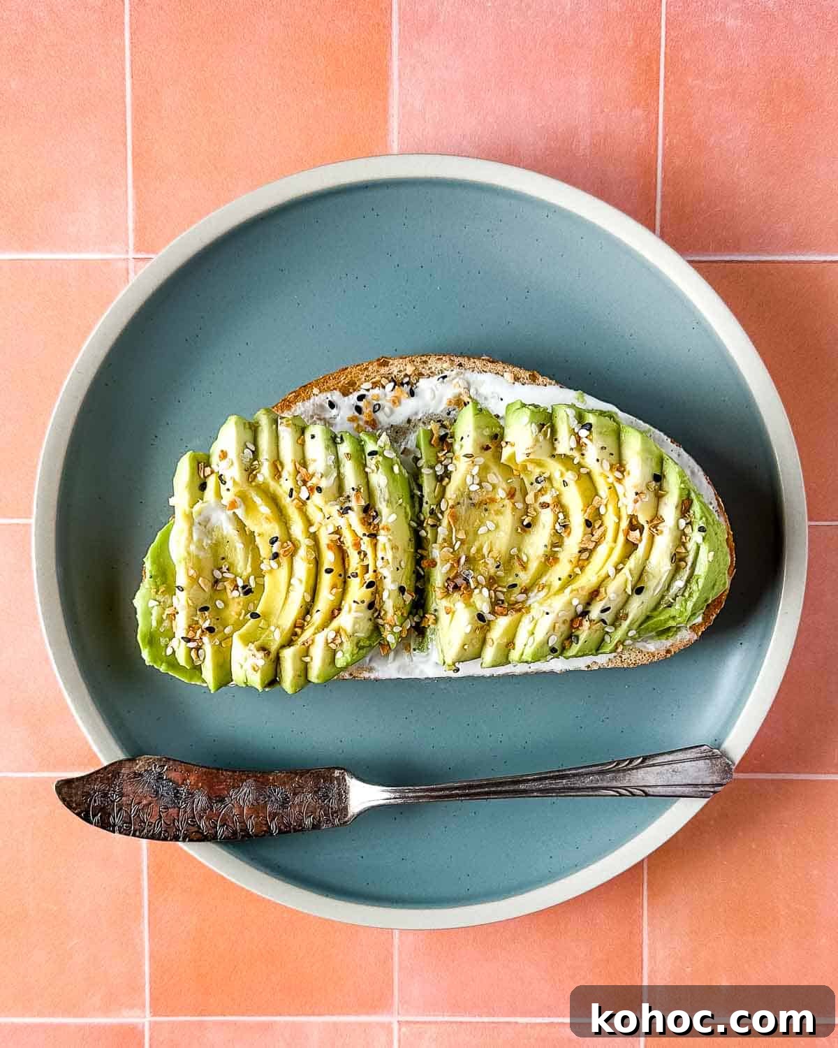Creamy Avocado Lime Tartine Recipe for Fresh Breakfast 2 an avocado tartine sits on a blue plate with a vintage silver knife over a peach tile background.