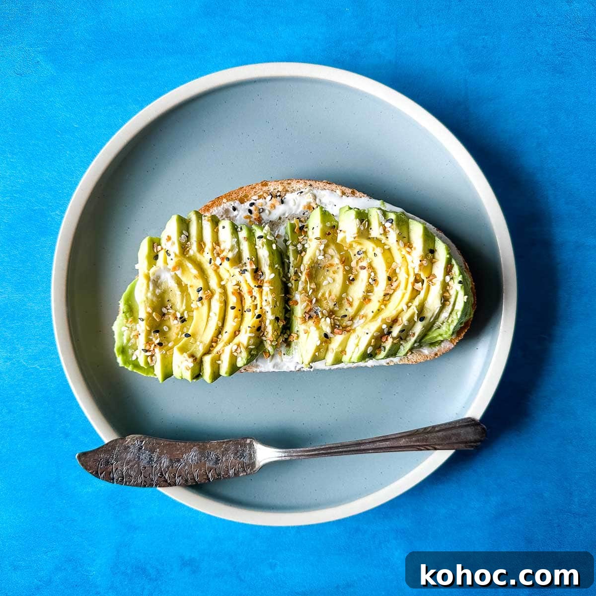 Creamy Avocado Lime Tartine Recipe for Fresh Breakfast 11 an avocado tartine sits on a light blue plate with a vintage silver knife over a blue darker background.