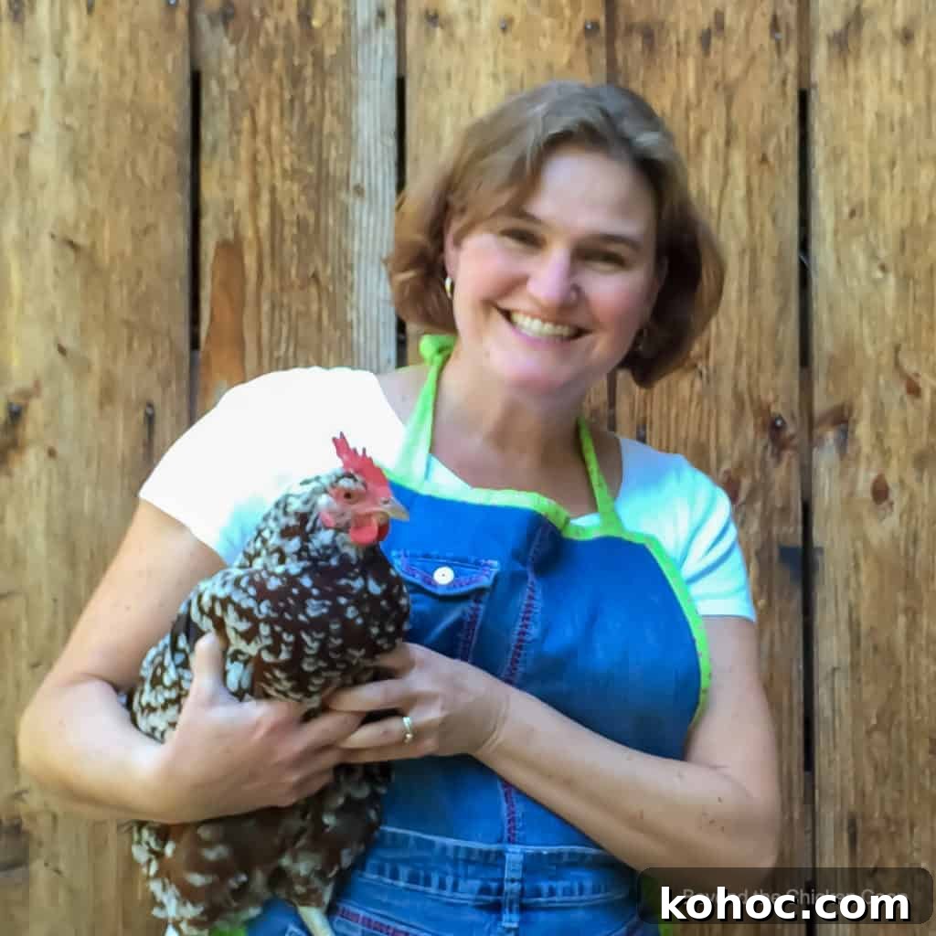 Campfire Fish Fry with Kathy Berget: Simple Outdoor Recipe 2 a woman with short brownish hard in a white t-shirt and blue apron holding a chicken in front of a wooden fence.