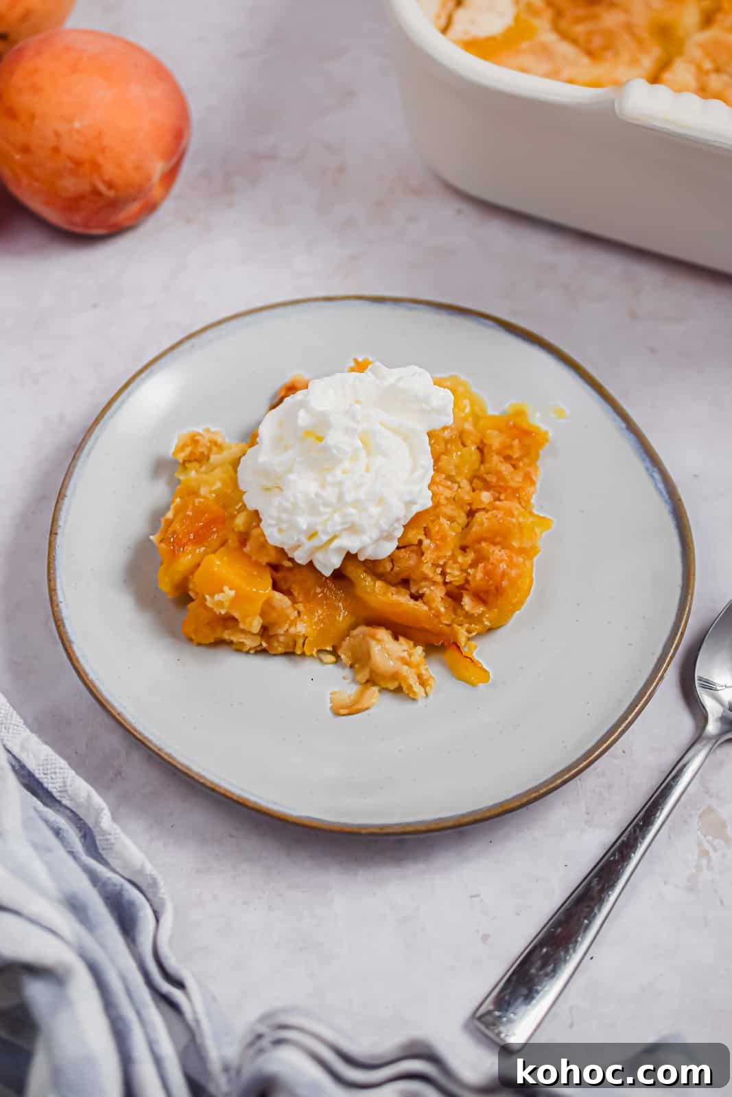 The peach cobbler is on a plate topped with whipped cream and peaches surrounding it.