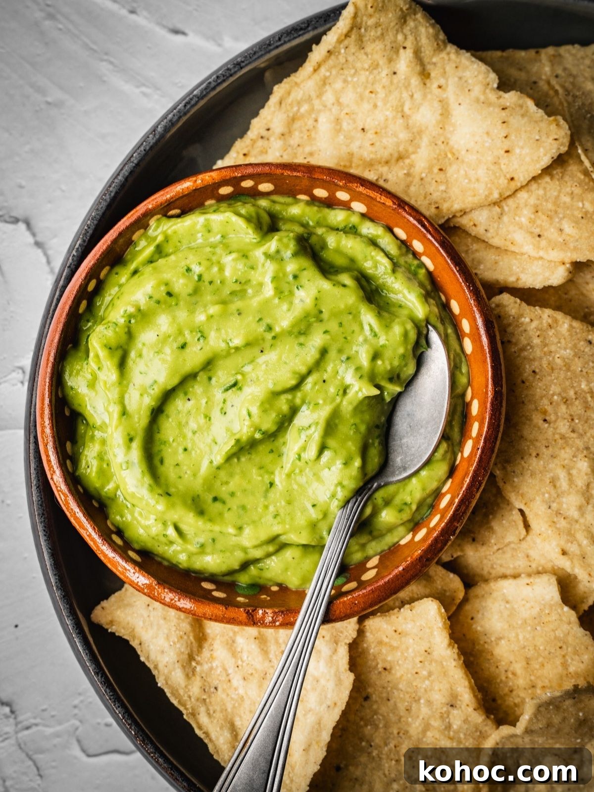 Avocado salsa in a bowl with a spoon and nacho chips on the side.