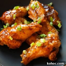 Crispy Honey Garlic Chicken Wings Recipe for Sticky, Savory Flavor 8 Honey Garlic Chicken Wings on a black plate with scallions on top.
