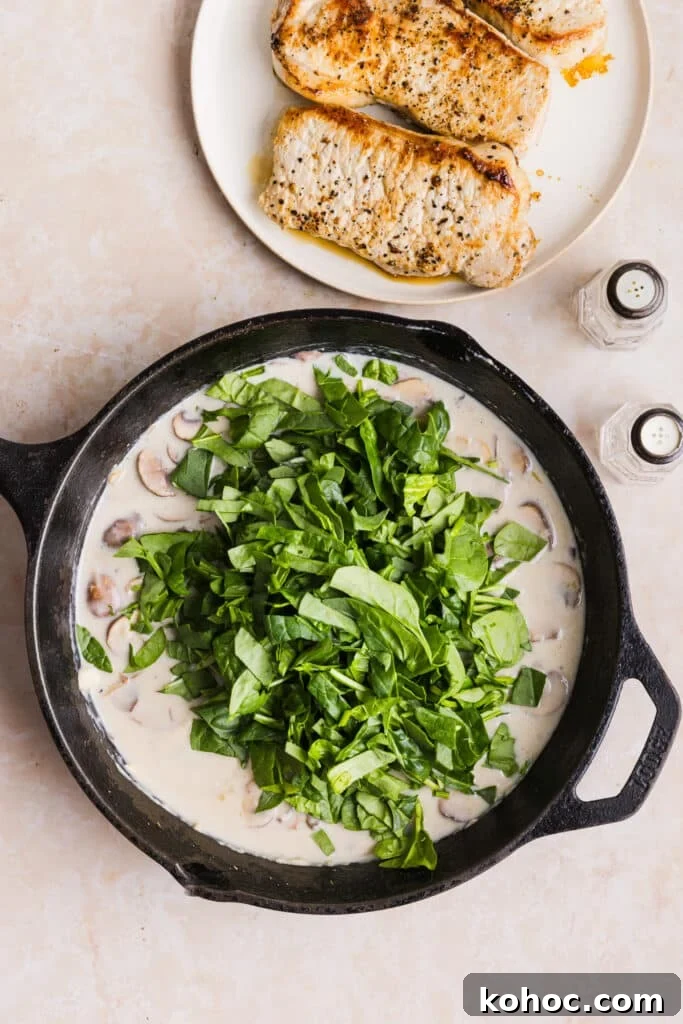 Creamy Garlic Pork Chops with Lighter Sauce 8 Spinach being added to a pan with a creamy sauce and mushrooms.
