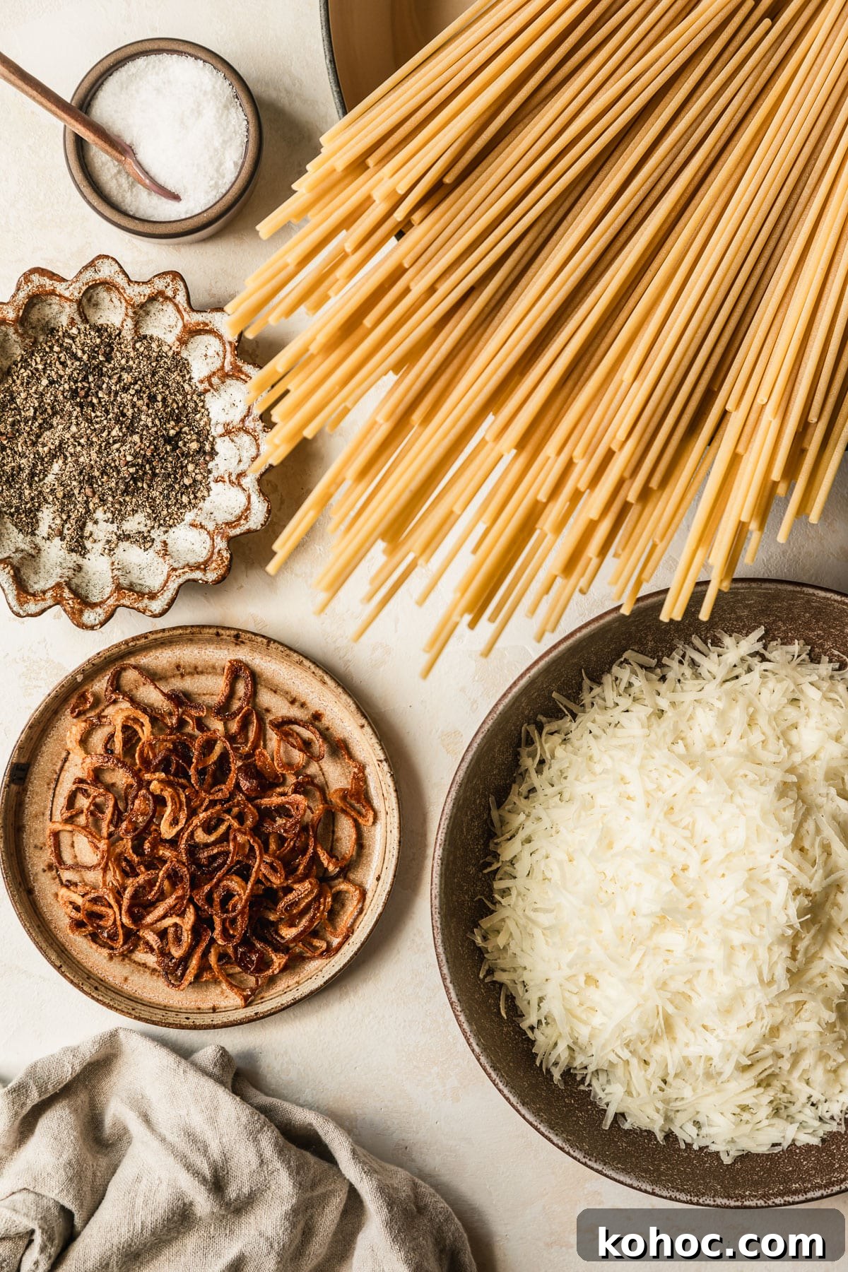 Crispy Shallot Bucatini Cacio e Pepe Recipe 3 Brown bowls of pasta, pepper, fried shallots, and Pecorino Romano on a tan counter.
