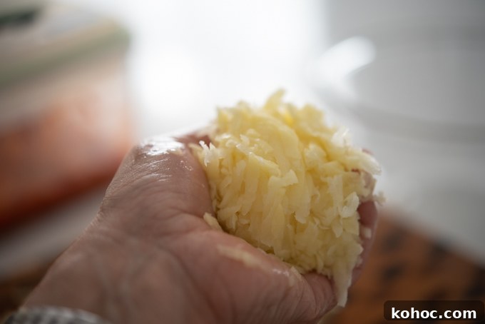 Cheesy Kimchi Potato Pancakes Recipe for Crispy, Flavorful Korean-Style Pancakes 5 Hand squeezing out to remove water from potatoes.