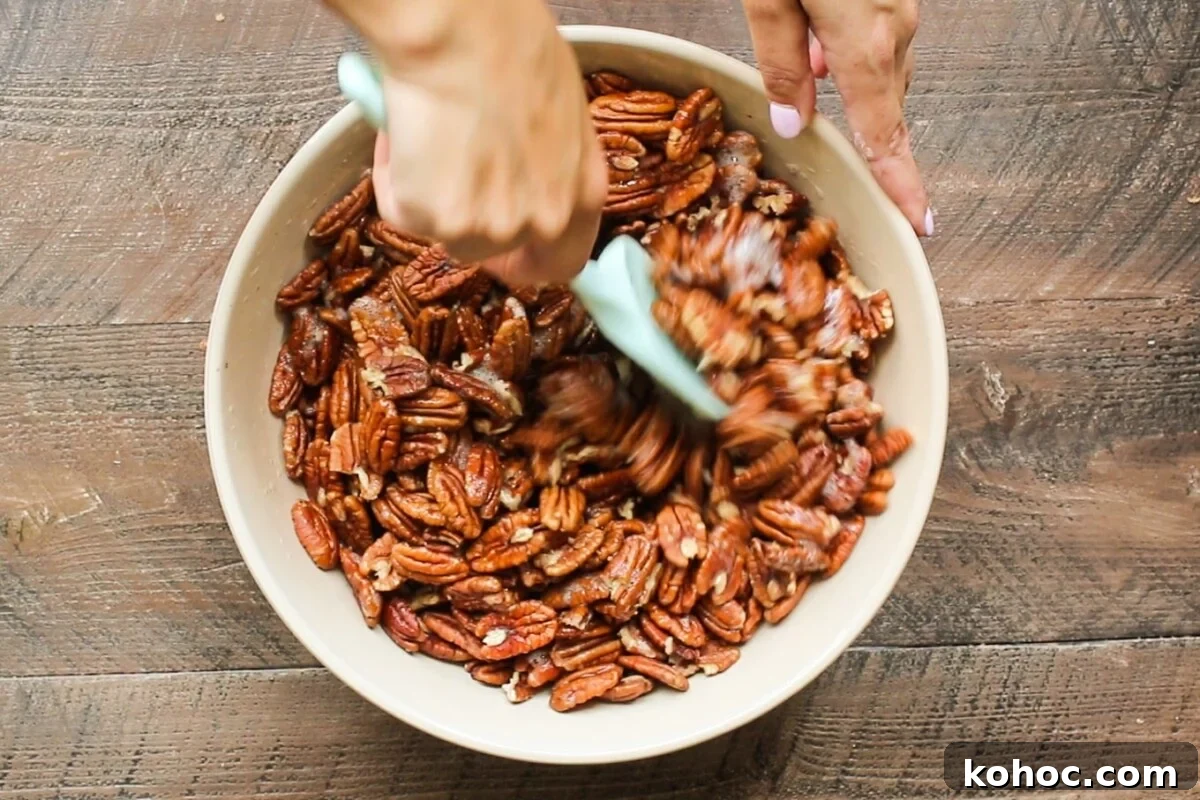 Perfectly Candied Pecans in the Slow Cooker (Simple Recipe) 4 pecans being stirred with a green spatula.