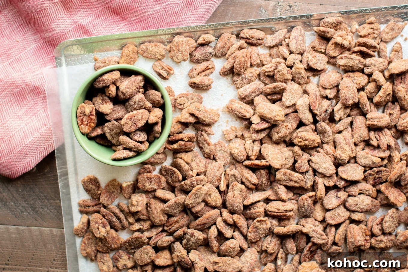 Perfectly Candied Pecans in the Slow Cooker (Simple Recipe) 7 pecans on a wax paper-lined sheet tray. Some pecans in a small green bowl.