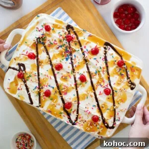 Banana Split Ice Cream Sandwich Cake Recipe for Summer Parties 14 A large ice cream sundae dessert in a white dish, topped with whipped cream, rainbow sprinkles, maraschino cherries, chocolate syrup, and caramel sauce. Surrounding bowls hold cherries, sprinkles, and syrup.