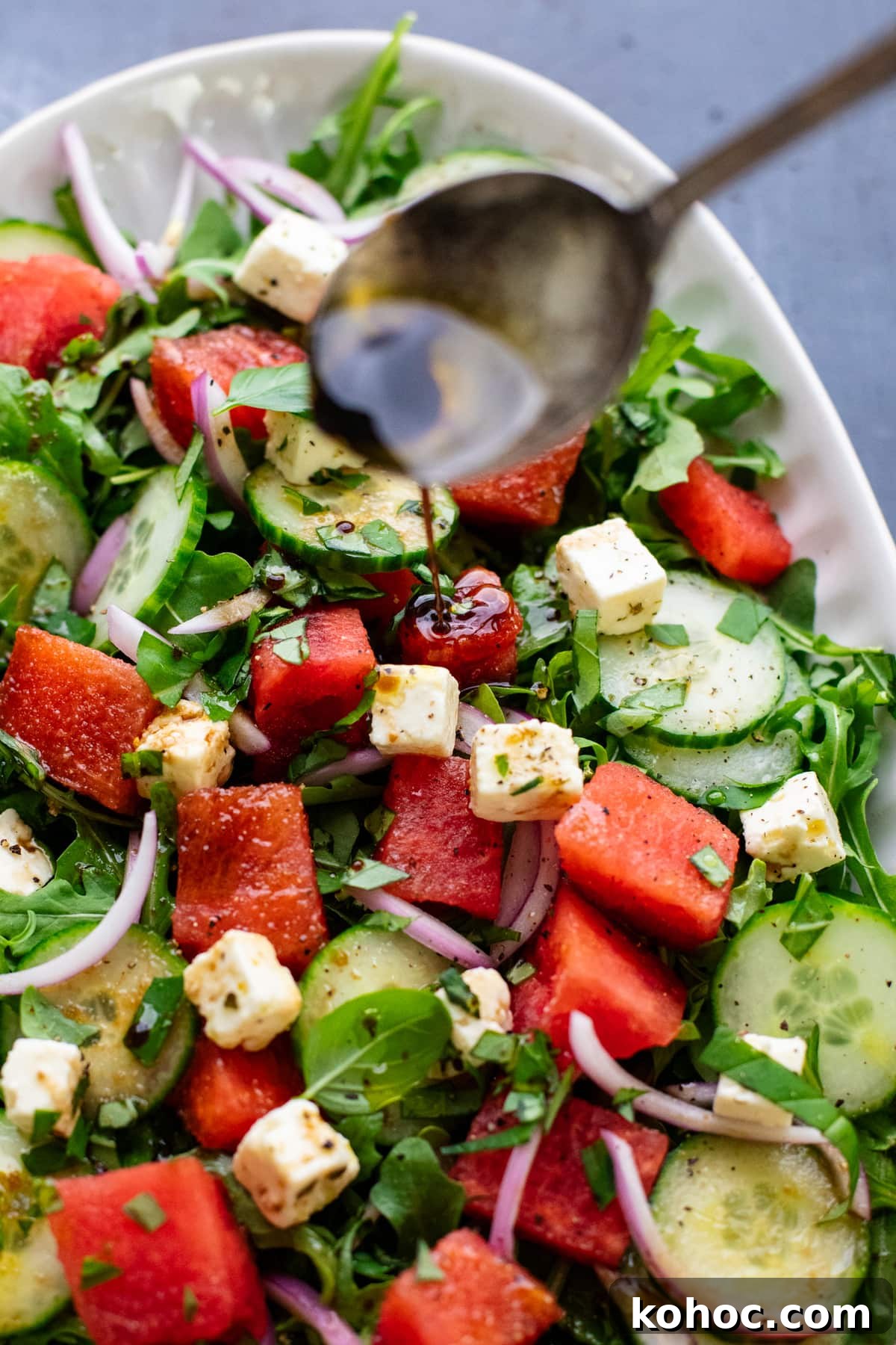 Watermelon, Feta & Basil Salad with Balsamic Glaze 5 spoon drizzling dressing over watermelon salad.