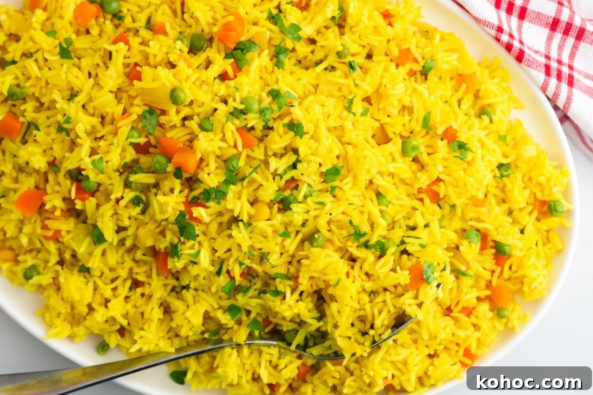 29 Tasty Meals You Can Make with Frozen Vegetables 11 A large white plate filled with vibrant yellow vegetable fried rice made using frozen vegetables, garnished with chopped herbs, served with a fork on the side.