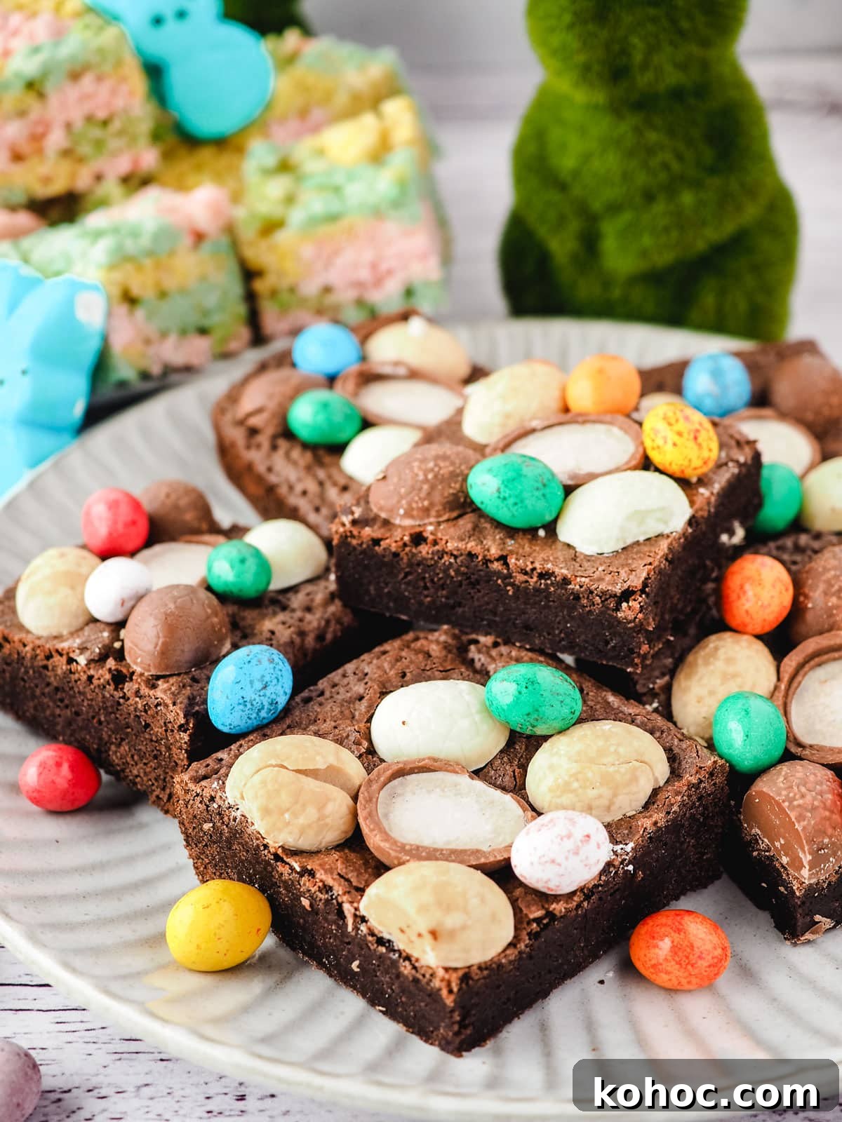 Easter brownies decorated with Easter eggs on a plate, with Easter decorations in the background.
