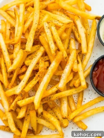 A plate of cooked French fries with sides of ketchup and mayonnaise.