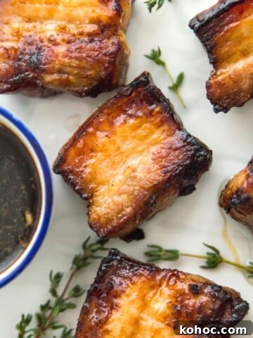 Cooked pork belly pieces on a plate with a side of soy sauce.