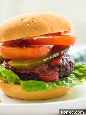 A burger in a bun topped with tomato slices, lettuce, ketchup and pickles.