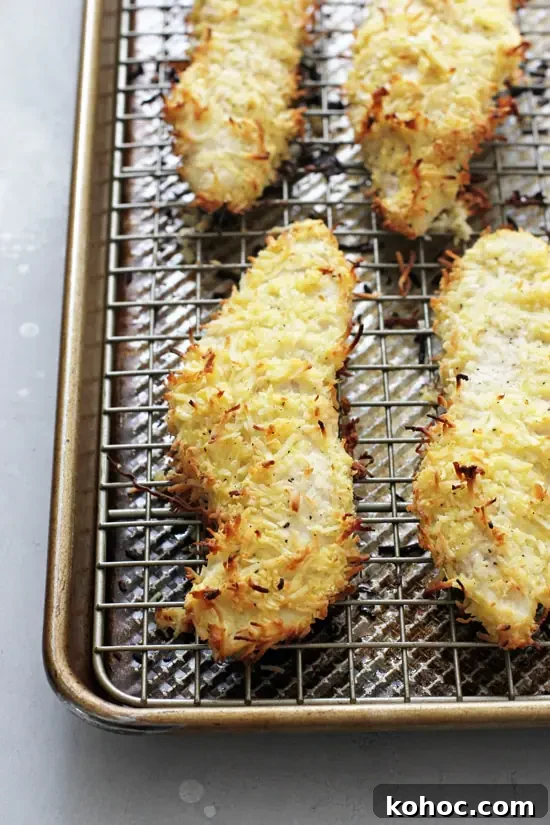 This weeknight baked coconut crusted chicken makes for an easy and healthy meal! With an almond flour coconut crust, a sticky apricot dipping sauce and just 30 minutes of your time required. Gluten free and dairy free. Several Coconut Chicken Strips on a baking sheet.