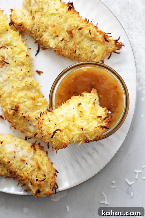 These coconut chicken tenders make for an amazing weeknight dinner that can’t be beat! With an almond flour coconut crust and a sticky apricot dipping sauce, they’re baked in the oven for a healthy meal. Gluten free and dairy free. Baked Coconut Chicken Tenders on a plate with one dunked in sauce.