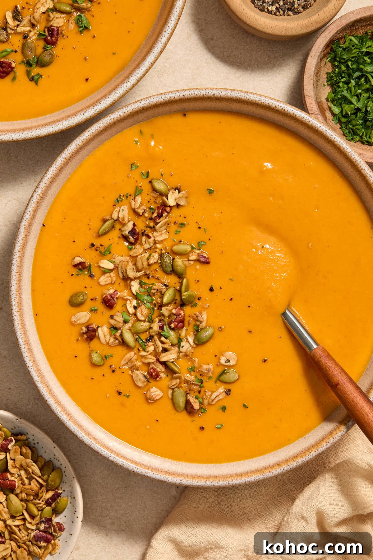 Roasted Red Pepper & Butternut Squash Soup — Dairy-Free Vegan Recipe 2 Close up of a bowl of soup with a spoon inserted into it and toppings on the side.