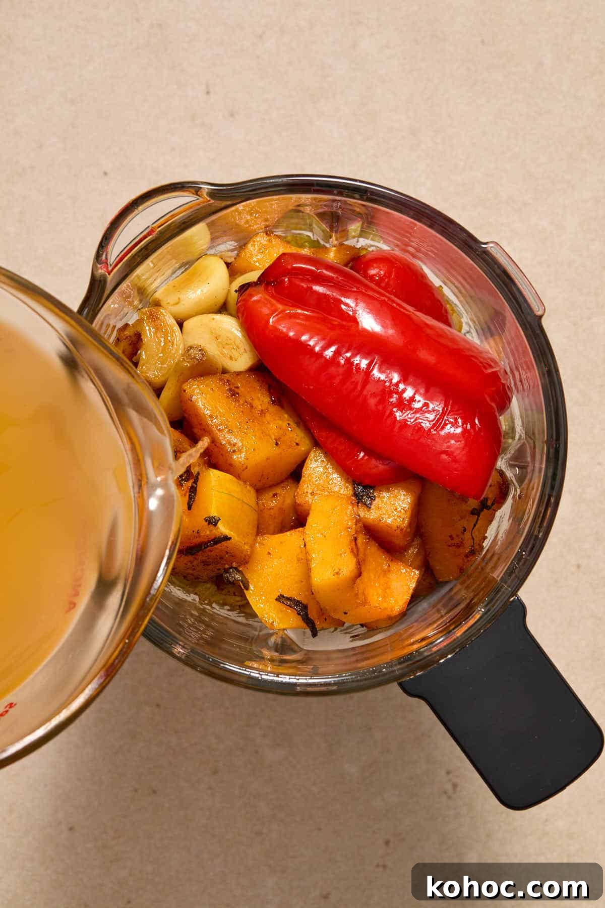 Roasted Red Pepper & Butternut Squash Soup — Dairy-Free Vegan Recipe 7 Roasted soup ingredients in a blender with vegetable broth being poured in.