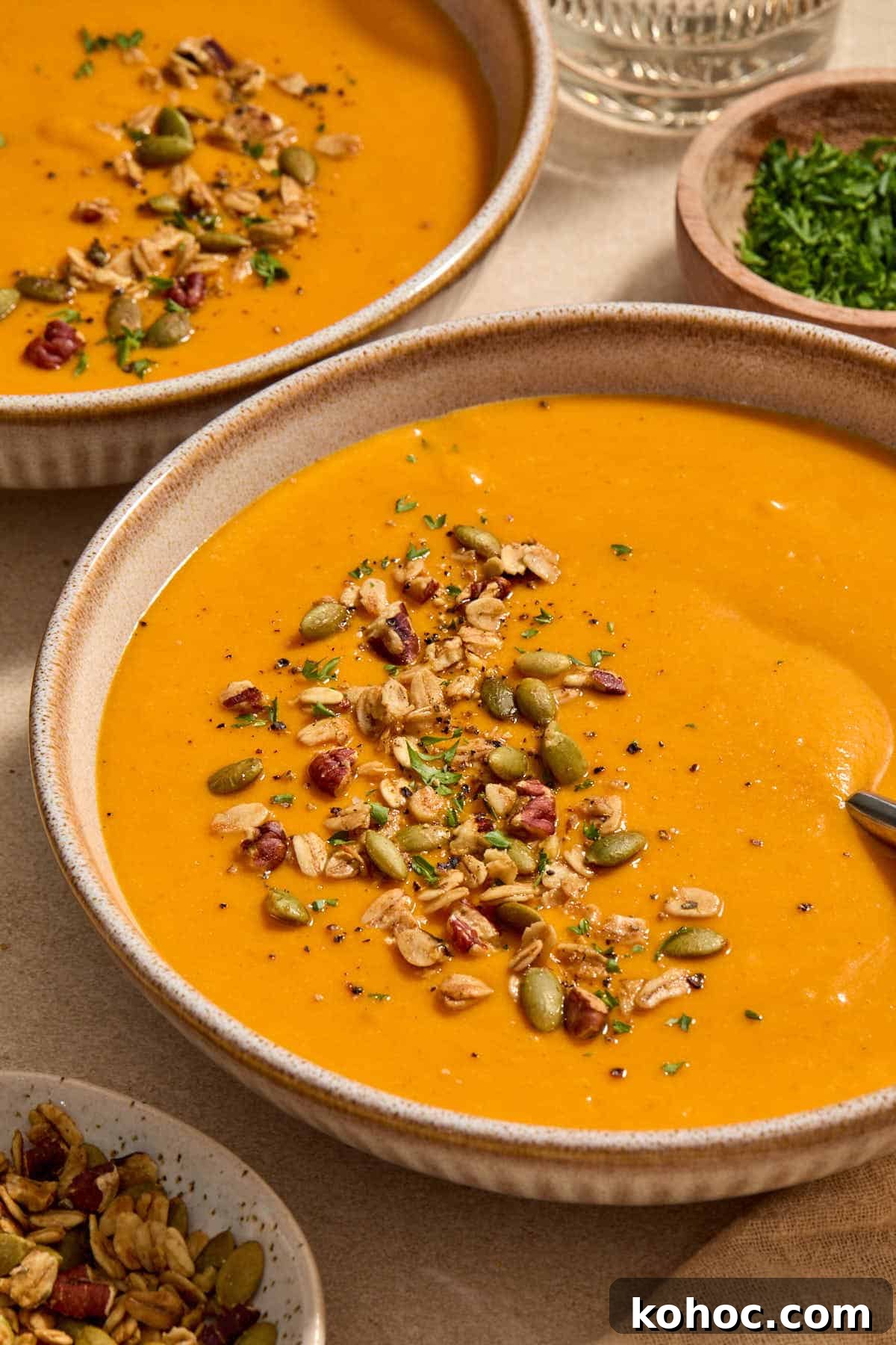 Roasted Red Pepper & Butternut Squash Soup — Dairy-Free Vegan Recipe 10 Angled view of a bowl of soup with another bowl in the background.
