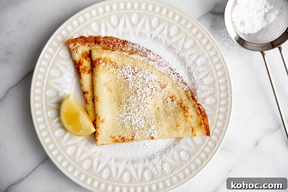 Crepes on a plate dusted with powdered sugar, with a lemon wedge alongside.