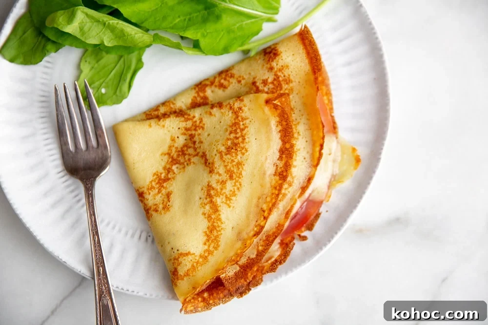 A ham and cheese crepe on a plate with a salad and fork. 