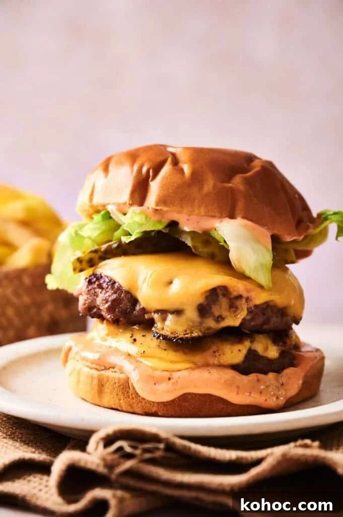 Savvy Slider Copycat Recipe: How to Make Restaurant-Style Sliders 2 A Copycat Savvy Slider double cheeseburger with lettuce, pickles, and sauce on a bun, served on a plate with fries in the background.