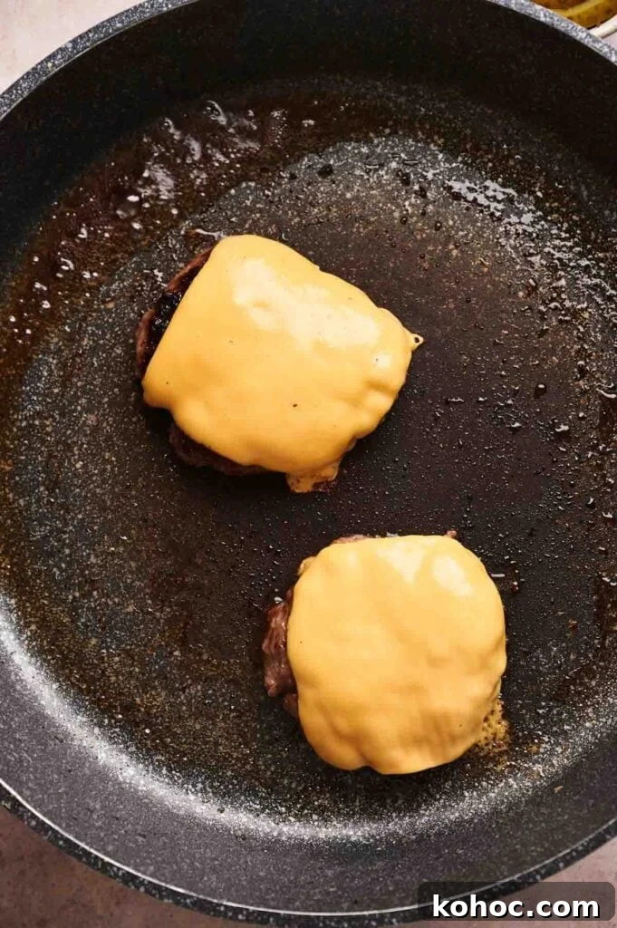 Savvy Slider Copycat Recipe: How to Make Restaurant-Style Sliders 5 Two hamburger patties topped with melted cheese slices sizzle in a nonstick frying pan, perfect for making a Copycat Savvy Slider at home.