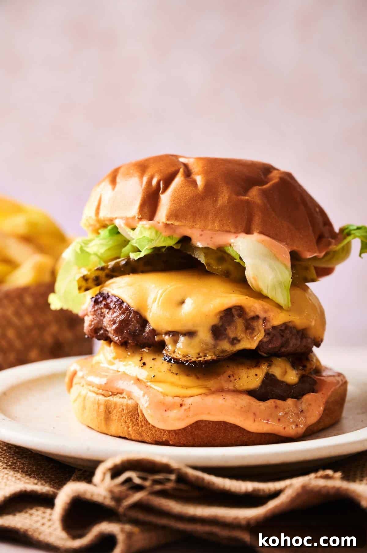 Savvy Slider Copycat Recipe: How to Make Restaurant-Style Sliders 7 A Copycat Savvy Slider double cheeseburger with lettuce, pickles, and sauce on a bun, served on a plate with fries in the background.