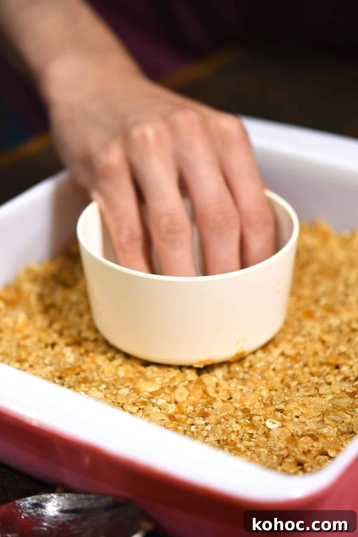 Chewy Apricot and Walnut Granola Bars 6 using a measuring cup to pack granola into baking dish