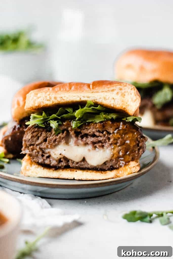 Juicy Lucy Lamb Burger Recipe: Melted Cheese Inside Every Bite 2 A burger cut on half sitting on a plate, with cheese oozing out, and arugula and fig preserves on the burger