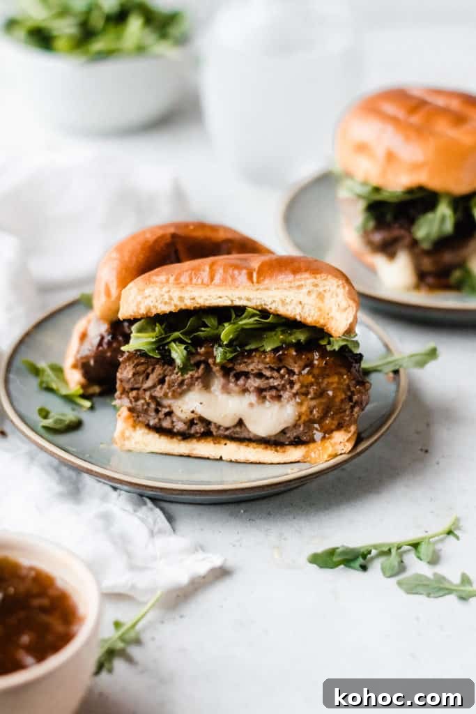 Juicy Lucy Lamb Burger Recipe: Melted Cheese Inside Every Bite 5 A lamb burger cut in half, with cheese oozing out, topped with fig preserves and arugula, with a brioche bun, on a blue plate