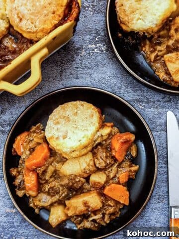 Overhead of a black plate of beef cobbler, with the corner of the serving dish in the background.