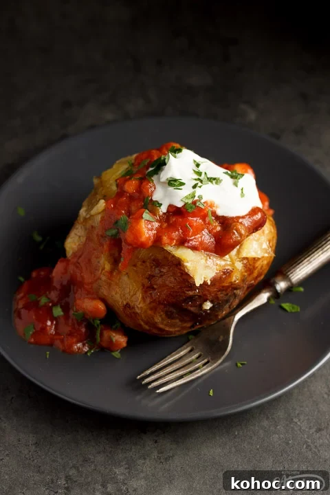 Slow Cooker Baked Jacket Potatoes Recipe 7 A slow cooker jacket potato on a grey plate topped with vegan chilli and vegan creme fraiche