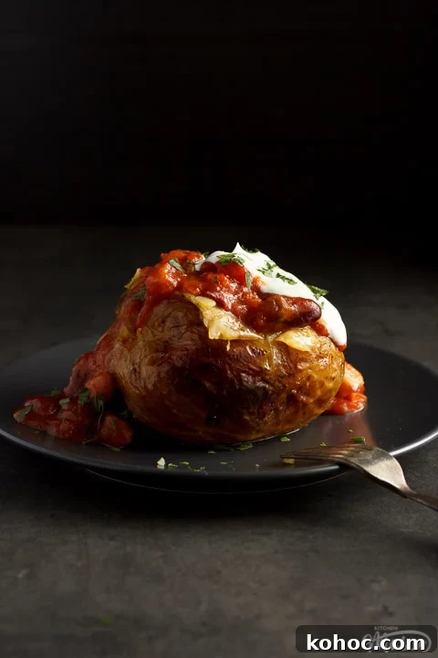 Slow Cooker Baked Jacket Potatoes Recipe 8 A slow cooker jacket potato on a grey plate topped with vegan chilli and vegan creme fraiche