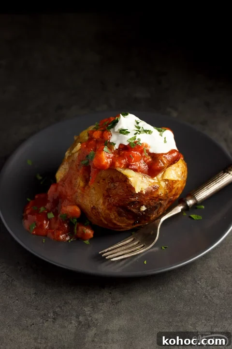 Slow Cooker Baked Jacket Potatoes Recipe 9 A slow cooker jacket potato on a grey plate topped with vegan chilli and vegan creme fraiche