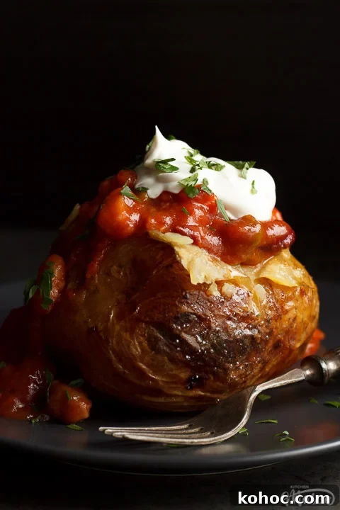 Slow Cooker Baked Jacket Potatoes Recipe 17 A slow cooker jacket potato on a grey plate topped with vegan chilli and vegan creme fraiche