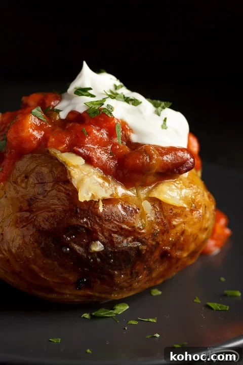 Slow Cooker Baked Jacket Potatoes Recipe 3 A slow cooker jacket potato on a grey plate topped with vegan chilli and vegan creme fraiche