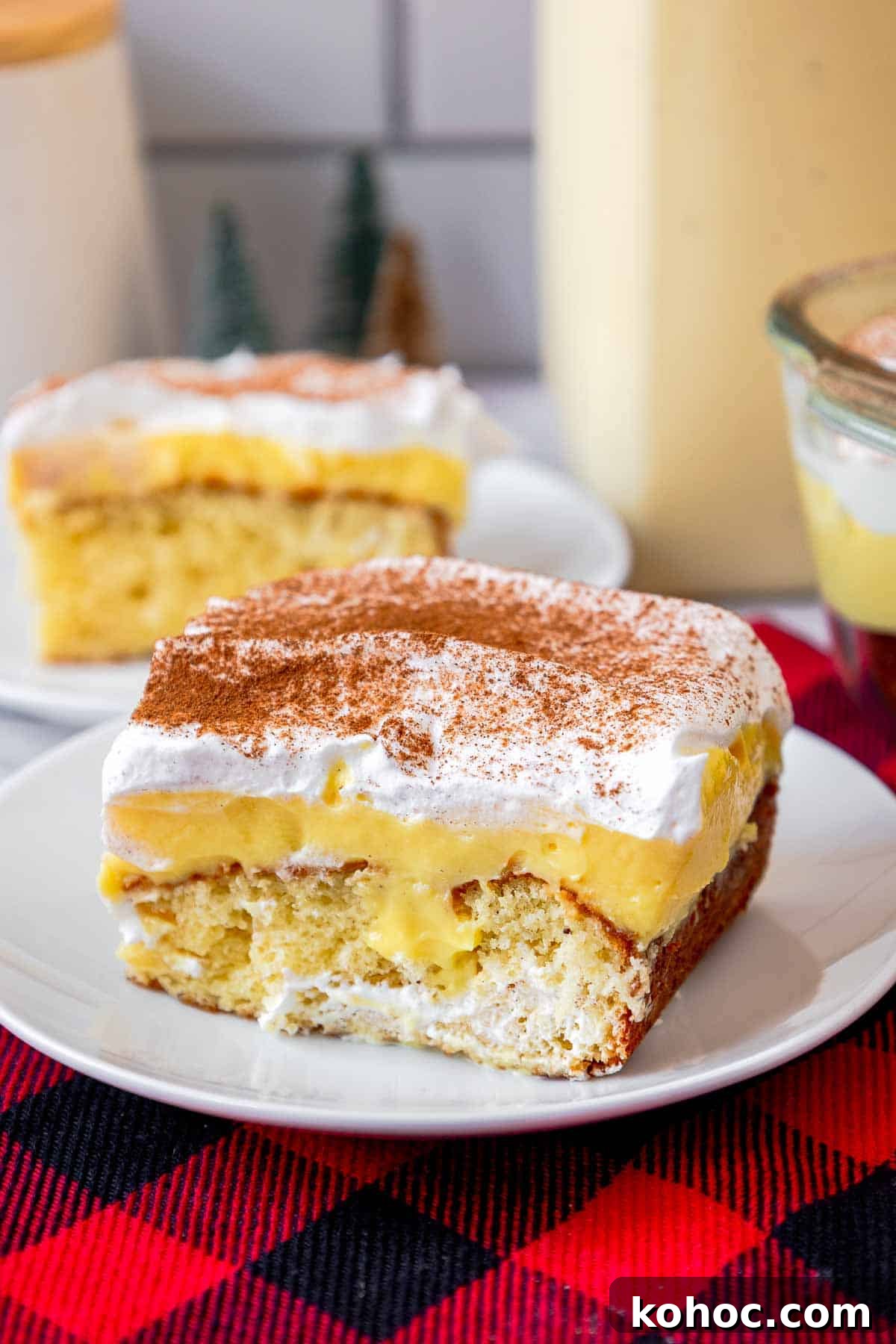 Slice of eggnog poke cake on a small plate showing butter cake layer, eggnog pudding layer, and whipped topping layer.