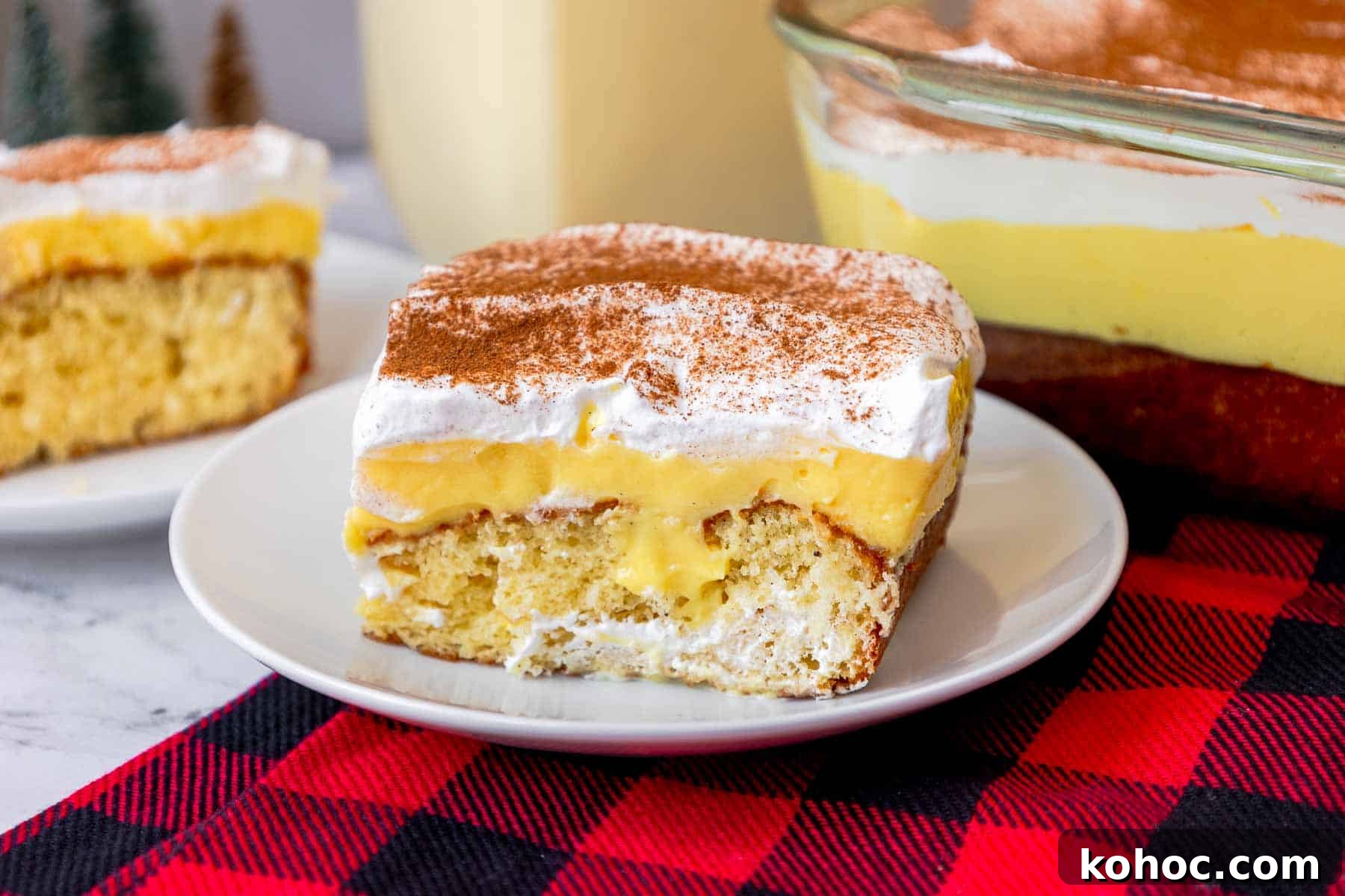 Slice of eggnog poke cake on a small plate showing butter cake layer, eggnog pudding layer, and whipped topping layer.