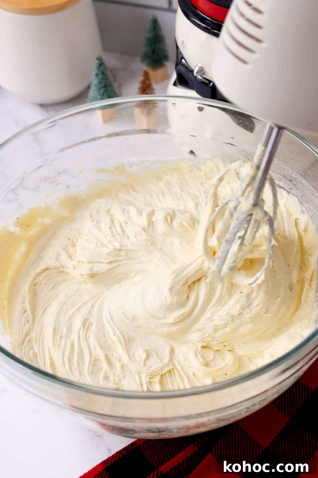 A mixing bowl of whipped eggnog butter cake mixture with electric beaters resting on the edge, ready to be added to the cake.