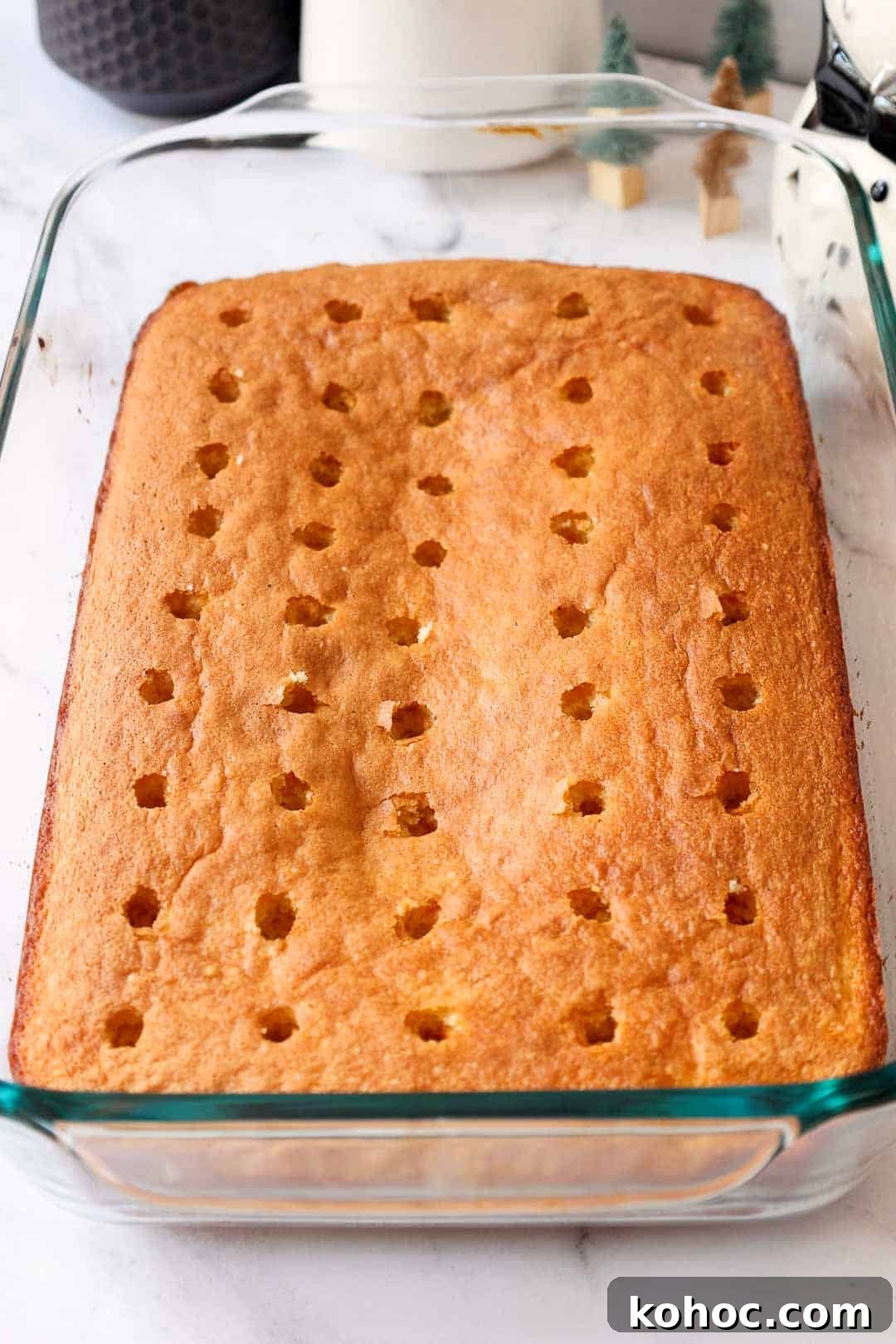 The baked butter cake layer with evenly spaced holes poked across the top, ready for the eggnog pudding to be poured in.