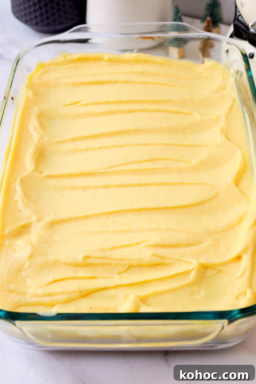 The glass baking dish filled with an even layer of eggnog pudding spread over the poked butter cake layer.