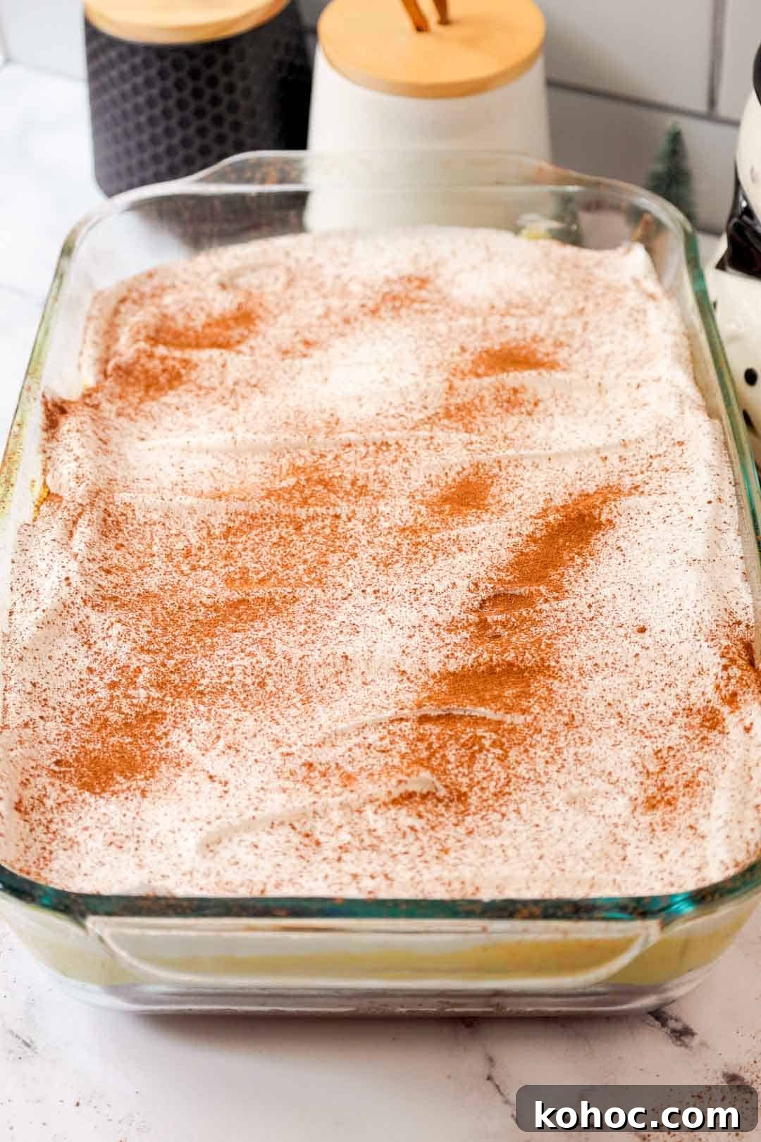 Finished eggnog poke cake topped with whipped cream and a generous dusting of cinnamon and nutmeg, chilled and ready to serve in a glass dish.