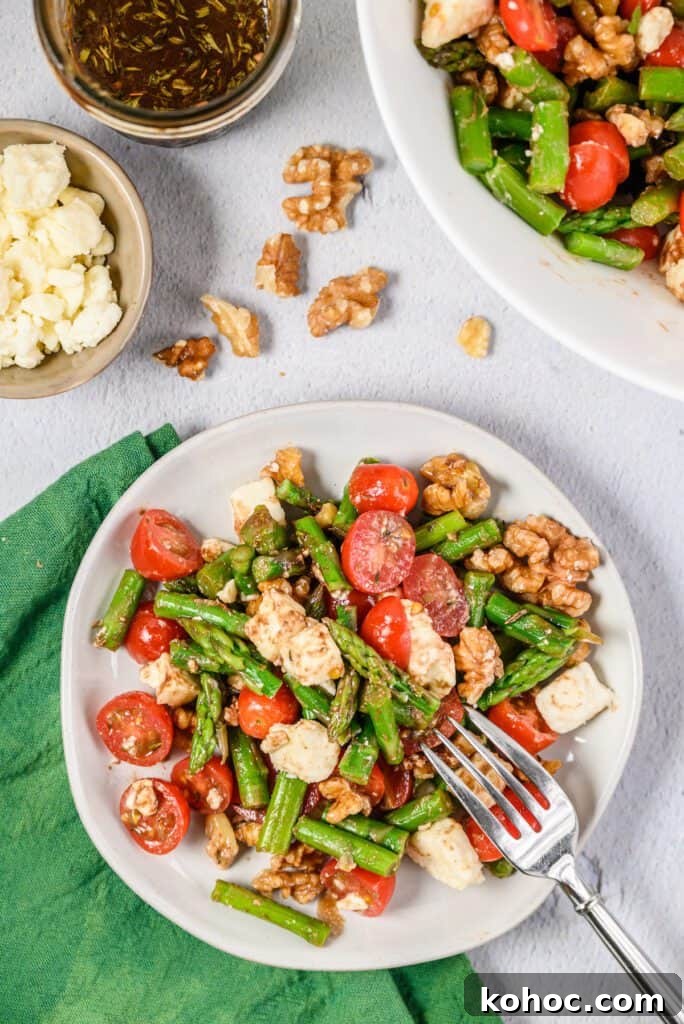 Chilled asparagus salad with tomatoes, crumbled feta cheese and walnuts on a plate drizzled with a balsamic dressing.