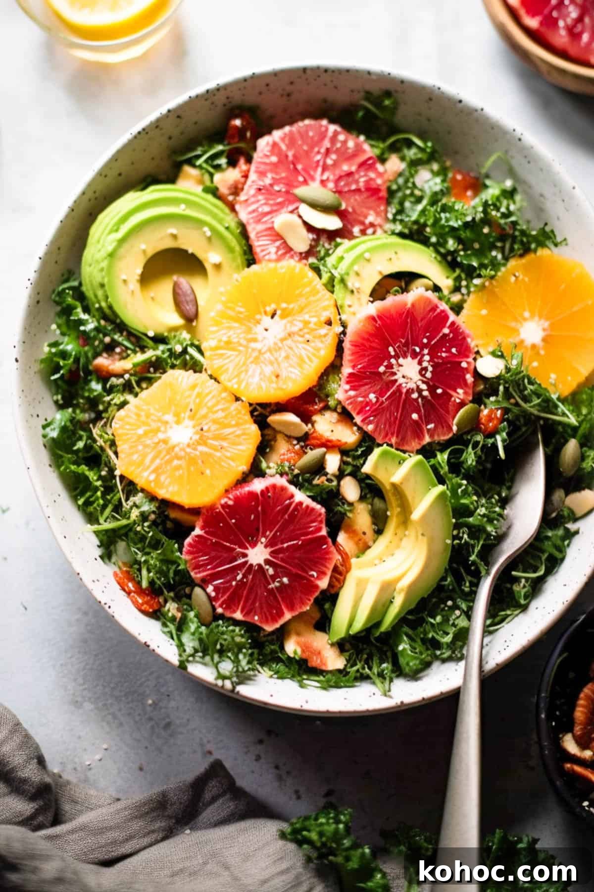 Kale citrus salad with oranges and avocado in a bowl with nuts and seeds.