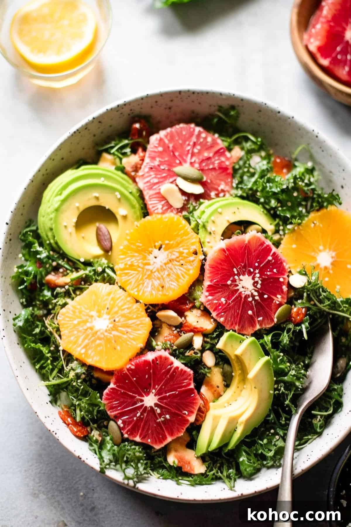 Kale citrus salad with oranges and avocado in a bowl with nuts and seeds.