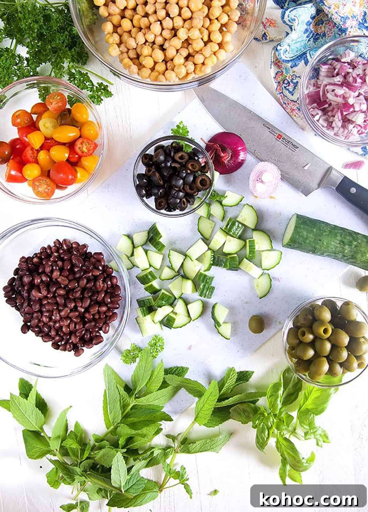 Mediterranean Chickpea Salad with Lemon, Herbs & Feta 4 Overhead shot of ingredients for chickpea salad on a white background with a knife.